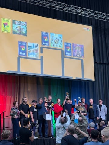 Preisträgerinnen und Preisträger des Deutschen Spiele Preises 2026 auf der Bühne mit den Spielecovern von Artengarten, Boss Fighters QR, Galactic Cruise und Toriki