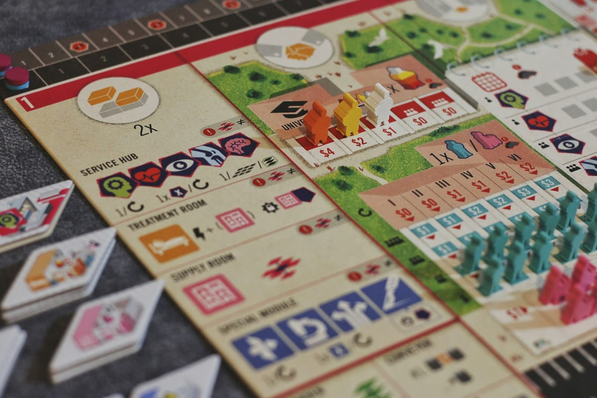 Symbolbild: Nahaufnahme eines aufgebauten Brettspiels mit Spielplänen, Karten und farbigen Spielfiguren.