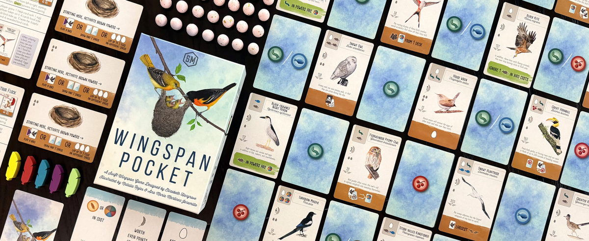 Spielschachtel von Wingspan Pocket mittig auf dunklem Tisch, umgeben von aufgefächerten Vogel- und Futterkarten des Spiels.