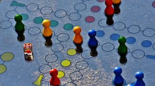 Bunte Holz-Pöppel und ein Würfel auf einem Spielbrett — Symbolbild zu den Nominierungen Spiel des Jahres 2026