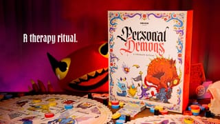 Verpackung von Personal Demons auf einem Spieltisch mit ausgelegten Karten und bunten Wertungsmarkern, im Hintergrund eine plüschartige rote Dämonenfigur, dramatisch rot beleuchtete Szene