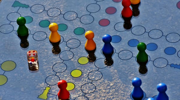 Bunte Holz-Pöppel und ein Würfel auf einem Spielbrett — Symbolbild zu den Nominierungen Spiel des Jahres 2026