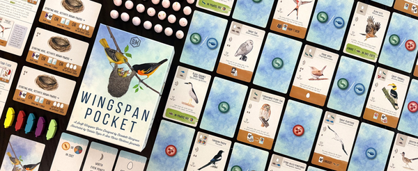 Spielschachtel von Wingspan Pocket mittig auf dunklem Tisch, umgeben von aufgefächerten Vogel- und Futterkarten des Spiels.
